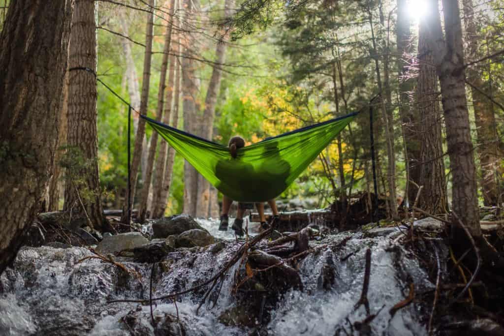 Zwei Menschen sitzen in grüner Hängematte im Wald über einem Wildbach