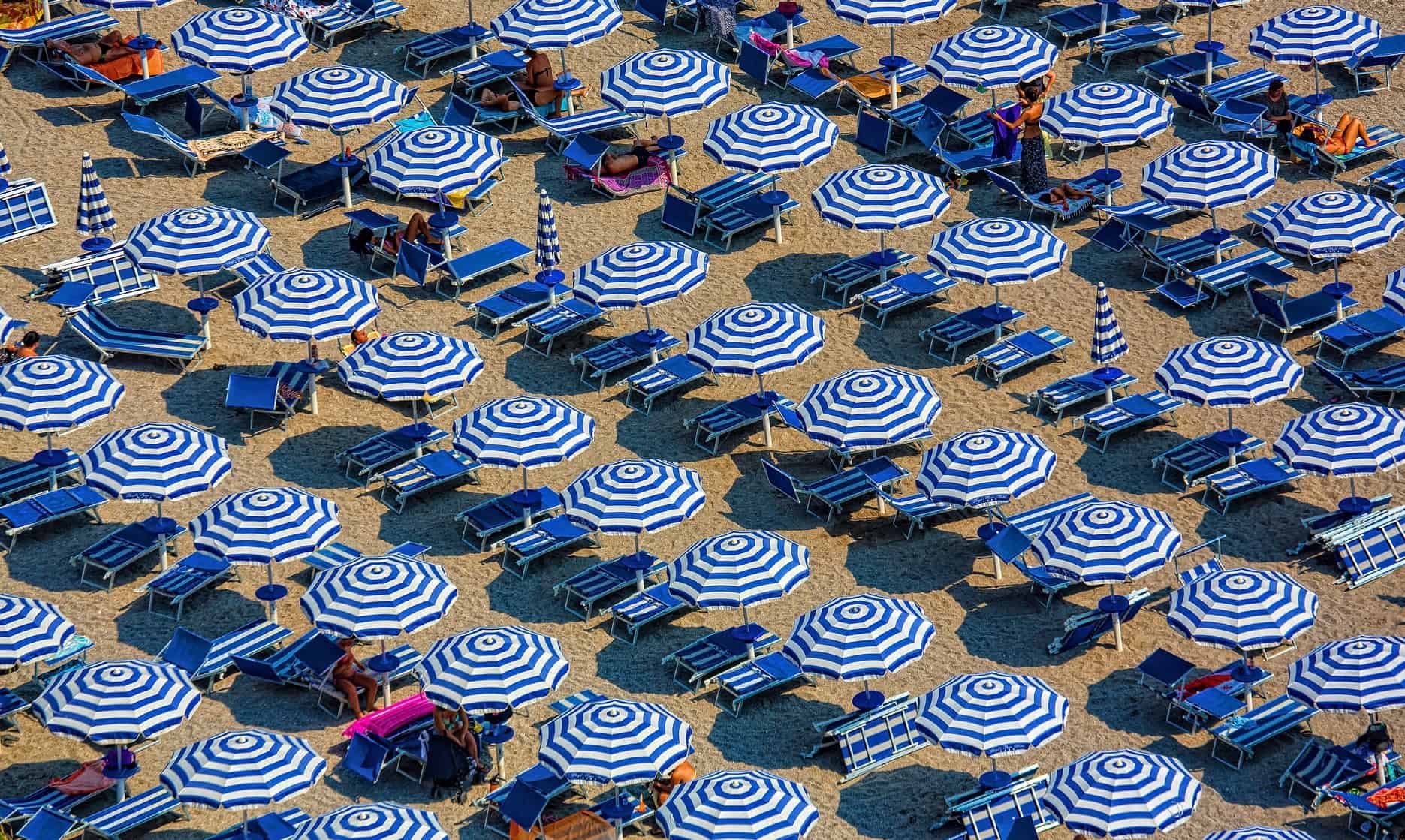 Strandabschnitt mit blauen Sonnenliegen und blau-weiß gestreiften Sonnenschirmen