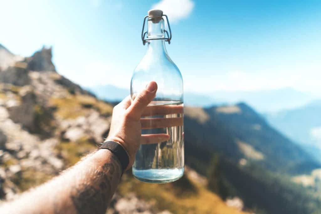 Mann zeigt Wasserflasche vor Berggipfeln im Hintergrund