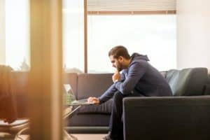 Mann sitzt auf Sofa und schaut in Notebook