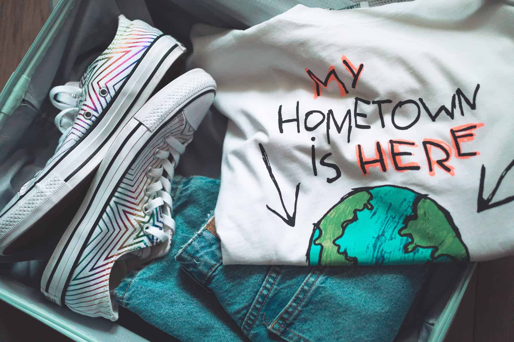 Bildausschnitt von kleinem offenen Koffer mit T-Shirt, Jeans und Turnschuhen